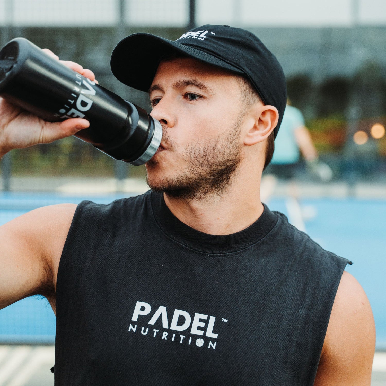 Padel player drinking carbohydrate sports drink during competitive match to maintain energy levels